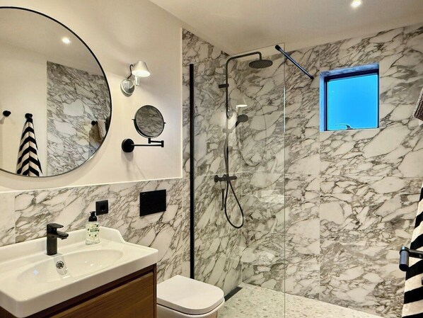 A modern bathroom with a marble wall, a round mirror, a sink with a soap dispenser, and a shower area. - Entire home in Grímsnes og Grafningshreppur, Iceland (Grímsnes og Grafningshreppur)