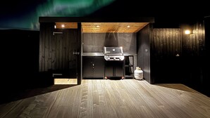 An outdoor kitchen area with a grill, wooden deck, and a view of the northern lights. - Entire home in Grímsnes og Grafningshreppur, Iceland (Grímsnes  og Grafningshreppur)