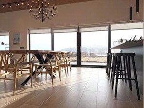Une pièce spacieuse comprenant une grande table à manger et des chaises, un coin bar et de grandes fenêtres donnant sur l’extérieur.
