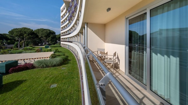 A modern hotel balcony with a curved railing, a seating area, and a view of the surrounding greenery.