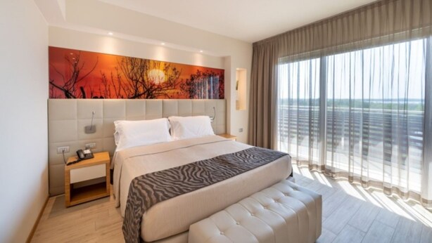 Habitación de hotel moderna con una cama grande, una mesita de noche, un teléfono y vistas al exterior a través de amplias ventanas.