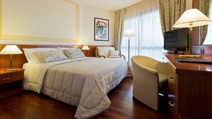 Une chambre d’hôtel avec un lit, un bureau, une chaise, une télévision et un tableau encadré au mur.