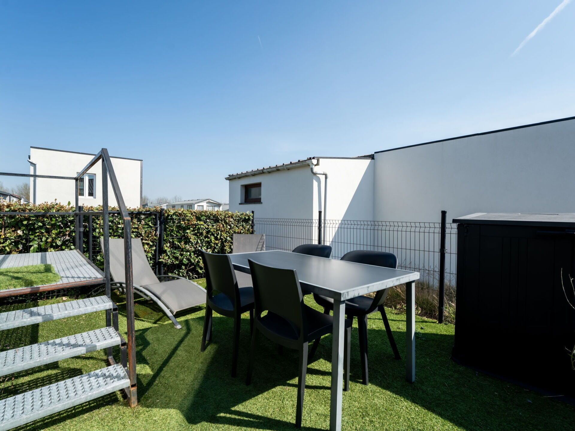 A patio with a table and chairs, a small play structure, and a black storage unit.