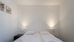 A hotel room with two single beds, each with a pillow and a rolled towel. There are wall-mounted light fixtures on either side of the beds. - Beautiful apartment in villa for 4 guests with WIFI, A/C, TV, terrace and pets allowed (Bruges)