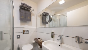 Ein modernes Badezimmer mit einer Duschkabine aus Glas, einem weißen Waschbecken mit Chromarmatur und einer Toilette.
