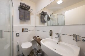 Un baño moderno con cabina de ducha de vidrio, un lavamanos blanco con grifo cromado y un inodoro.