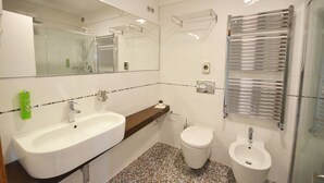 Ein modernes Badezimmer mit einem weißen Waschbecken, einer Toilette und einem Bidet. Über dem Waschbecken befindet sich ein Spiegel und an der Wand ein Handtuchhalter.