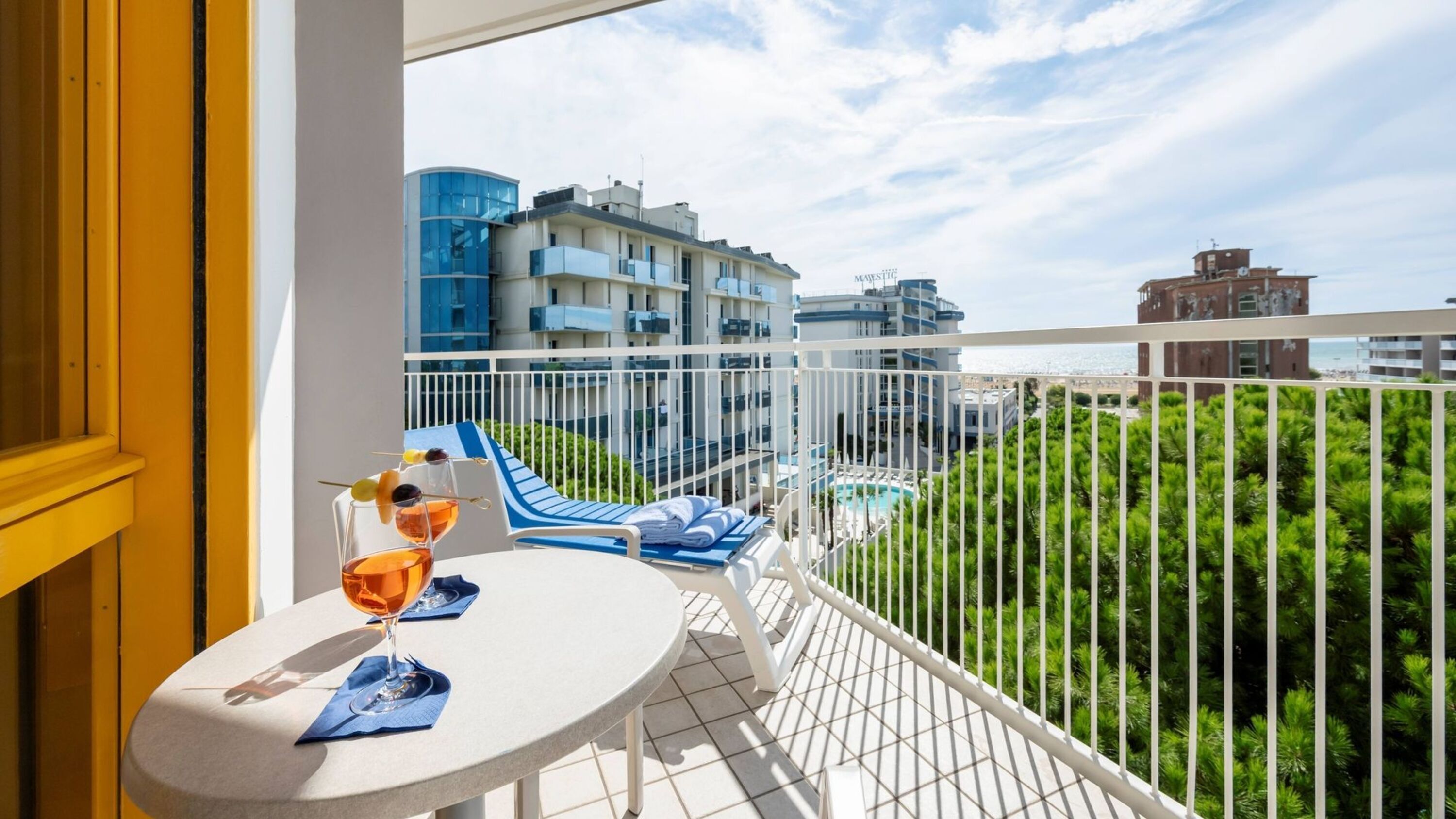Un balcon avec une table, deux verres de vin et une vue sur une piscine et des immeubles.