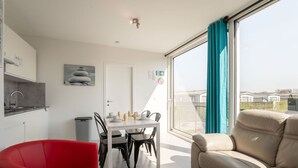 Una sala de estar moderna con un sofá, una mesa de comedor lista para cuatro comensales y una cocina con un lavamanos y armarios.
