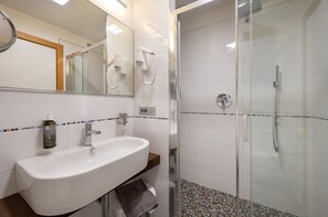 A modern bathroom with a white sink, a glass shower enclosure, and a mirror with hair dryers.