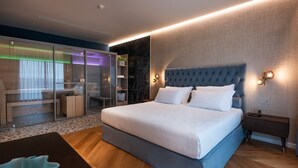A modern hotel room with a large bed, a desk, a glass-enclosed seating area, and a marble accent wall.
