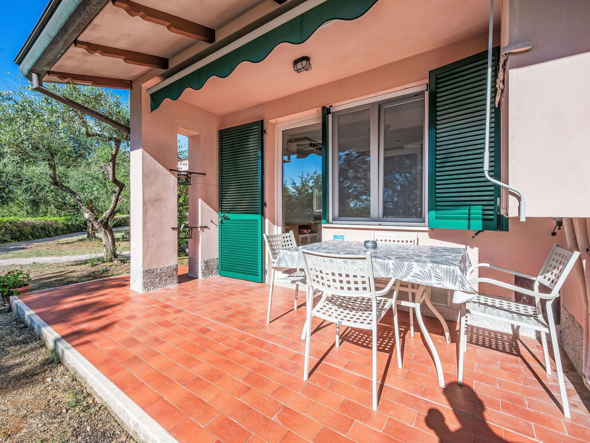 Une terrasse couverte avec une table et des chaises, une fenêtre avec des volets et une porte.