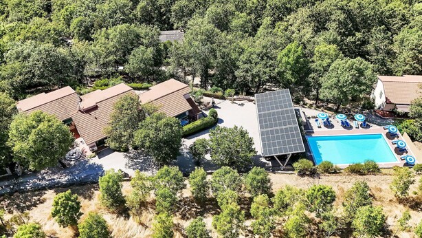 Vista aérea de una zona residencial con varias casas, una piscina con tumbonas y una instalación de paneles solares.