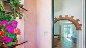 Una habitación con suelo de baldosas, una mesa de madera y una silla. Hay una planta en maceta con flores en la pared.