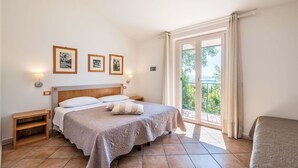 A bedroom with a bed, bedside tables, a chair, and a balcony with a view.