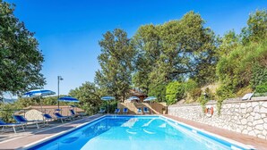 A swimming pool with lounge chairs and umbrellas, surrounded by trees and a stone wall.