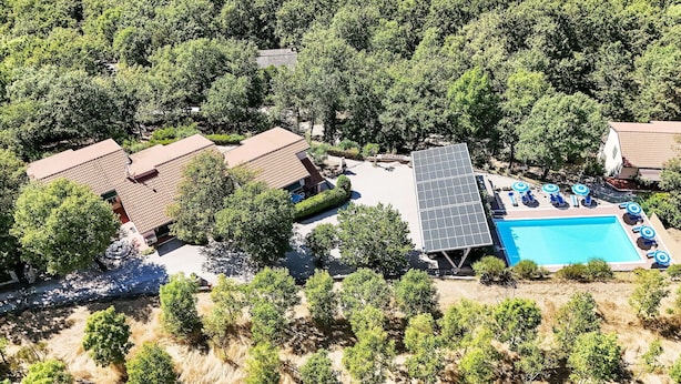 An aerial view of a residential area with multiple houses, a swimming pool with sun loungers, and a solar panel installation.