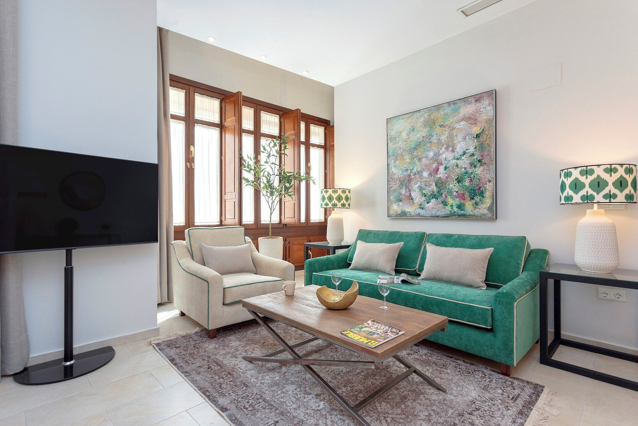 Een moderne woonkamer met een flatscreen televisie, een groene bank, een witte fauteuil en een salontafel.