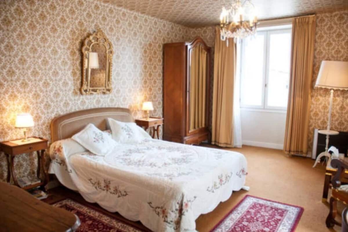 A bedroom with a large bed, wooden wardrobe, and a chandelier.