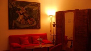 A room with a red sofa, a small table with a vase, a lamp, and a painting on the wall.