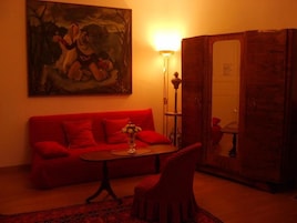 Quarto com um sofá vermelho, uma mesinha com um vaso, uma luminária e um quadro na parede.