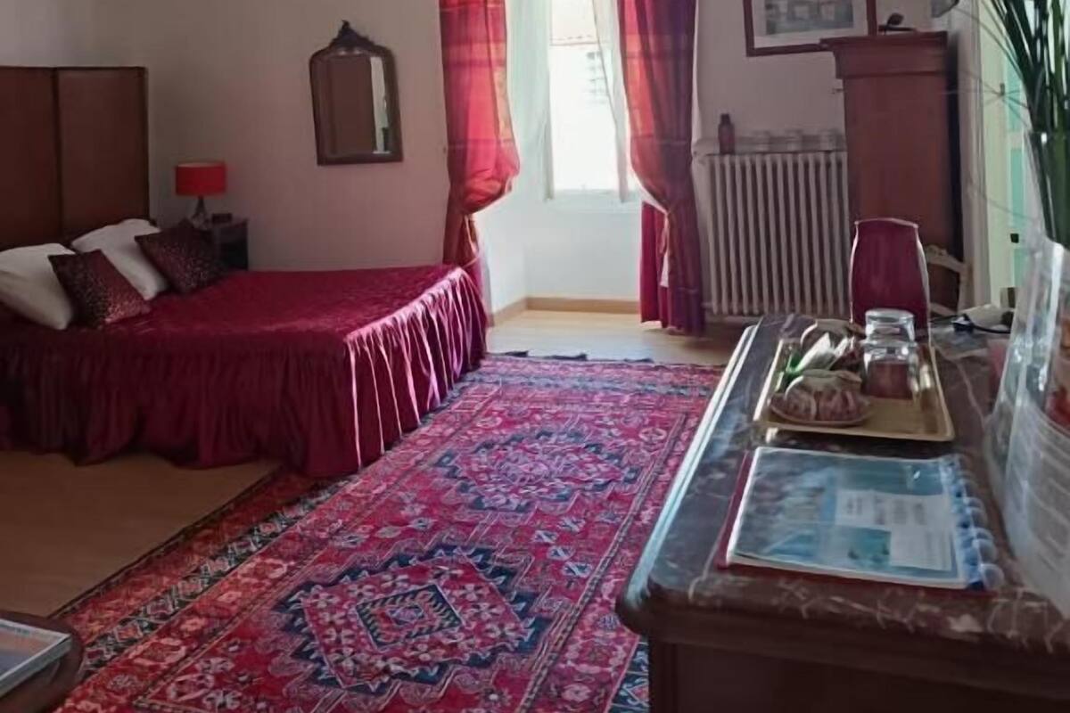A bedroom with a bed, a nightstand, a dresser, a radiator, and a window with curtains.