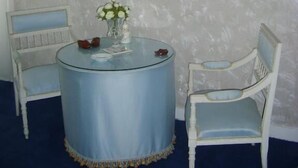 A room with a round table, two chairs, a vase with flowers, and a framed picture on the wall.
