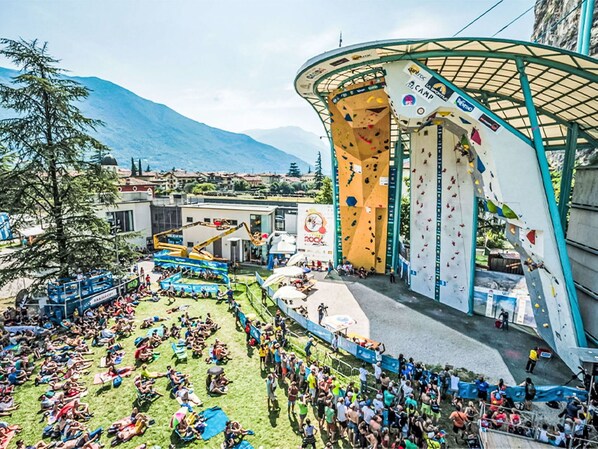 A climbing wall with multiple routes, a grassy area with people, and a mountainous backdrop.