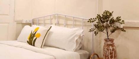A room with two beds, a small table with a vase, and a wicker chair.