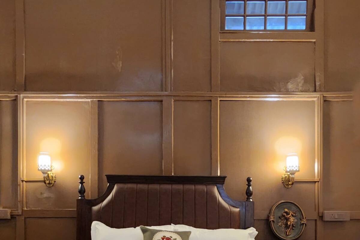 A large bed with a wooden headboard, two wall-mounted lamps, and a small table with a decorative item.