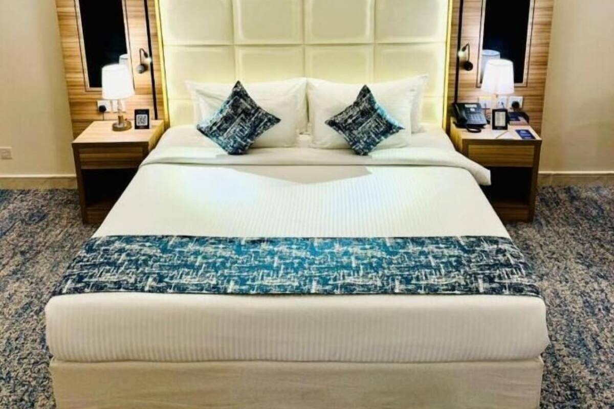 A hotel room with a large bed, two bedside tables with lamps, and a headboard with a light panel.