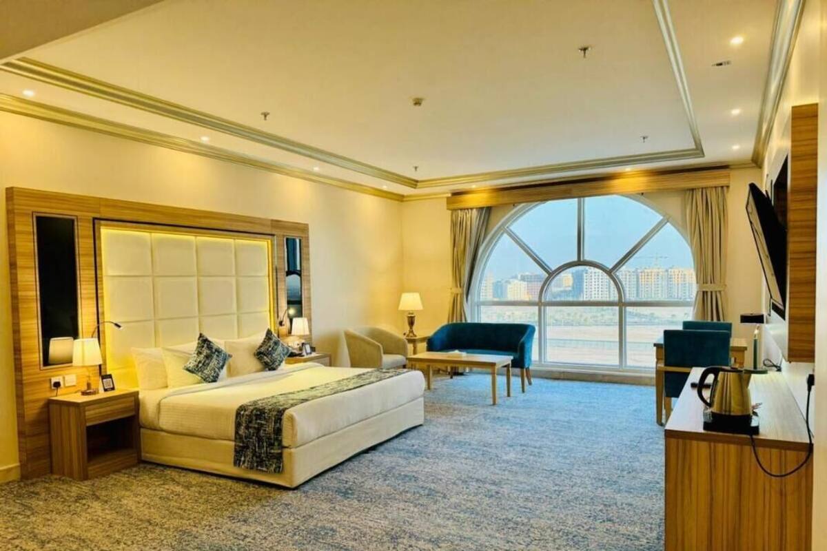 A hotel room with a large bed, a desk, a chair, and a view of the city through a large window.