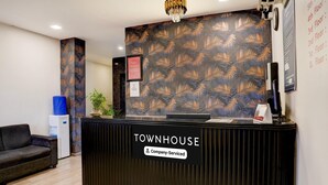 Un comptoir d’accueil portant l’inscription « TOWNHOUSE », agrémenté d’un panneau aux couleurs de l’entreprise, un canapé bleu, un distributeur d’eau et un mur orné d’un motif.