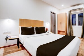 A hotel room with a bed, bedside table, and a wardrobe. - Cozy Stays Near Halasuru Metro Station (Bengaluru)