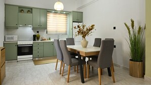 A modern kitchen with green cabinets, a dining table with chairs, and a vase with dried flowers. - El Dorado Corner (Chania)