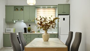 A modern kitchen with green cabinets, a white refrigerator, a marble table, and two grey chairs. - El Dorado Corner (Chania)