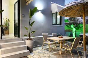 A patio with a table and chairs, a potted plant, and a thatched umbrella. - El Dorado Corner (Chania)