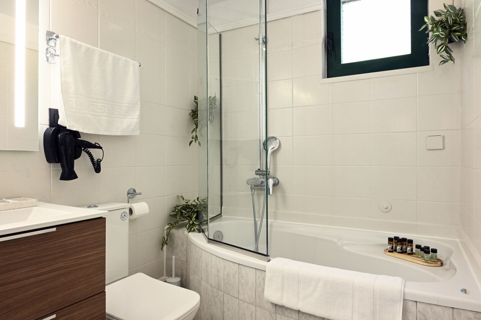 Ein modernes Badezimmer mit einer gläsernen Duschkabine, einer Badewanne mit einem Holztablett für Toilettenartikel und einem weißen Waschbecken mit einem Handtuch an der Wand.