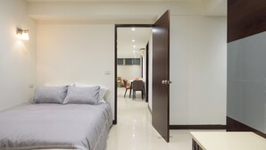 A hotel room with a bed, a bedside table, and a door leading to a dining area.