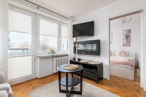 Un dormitorio moderno con un gran ventanal, un televisor de pantalla plana, una cama con ropa de cama rosa y una pequeña mesa redonda con individuales tejidos.