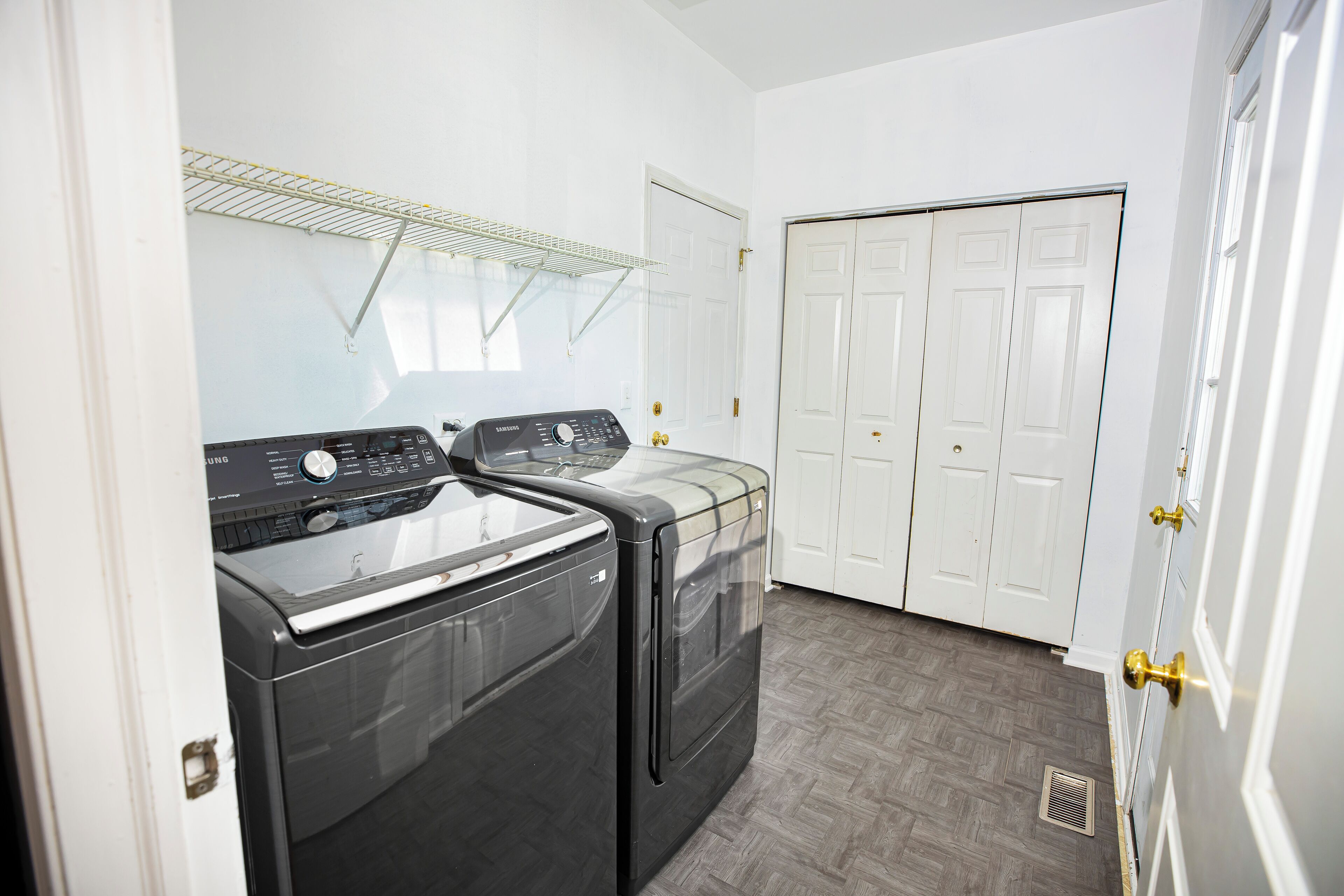 A laundry room with two front-loading washers and dryers, a metal drying rack, and a double door closet.