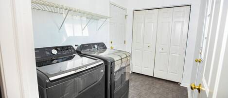 A laundry room with two front-loading washers and dryers, a metal drying rack, and a double door closet.