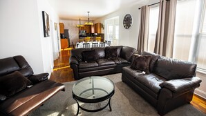 A modern living room with a sectional sofa, a glass coffee table, and a dining area in the background. - Serene 5-Bedroom Retreat, Oswego (Oswego)