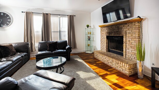A living room with a brick fireplace, leather sofas, a glass coffee table, and a large wall clock. - Serene 5-Bedroom Retreat, Oswego (Oswego)