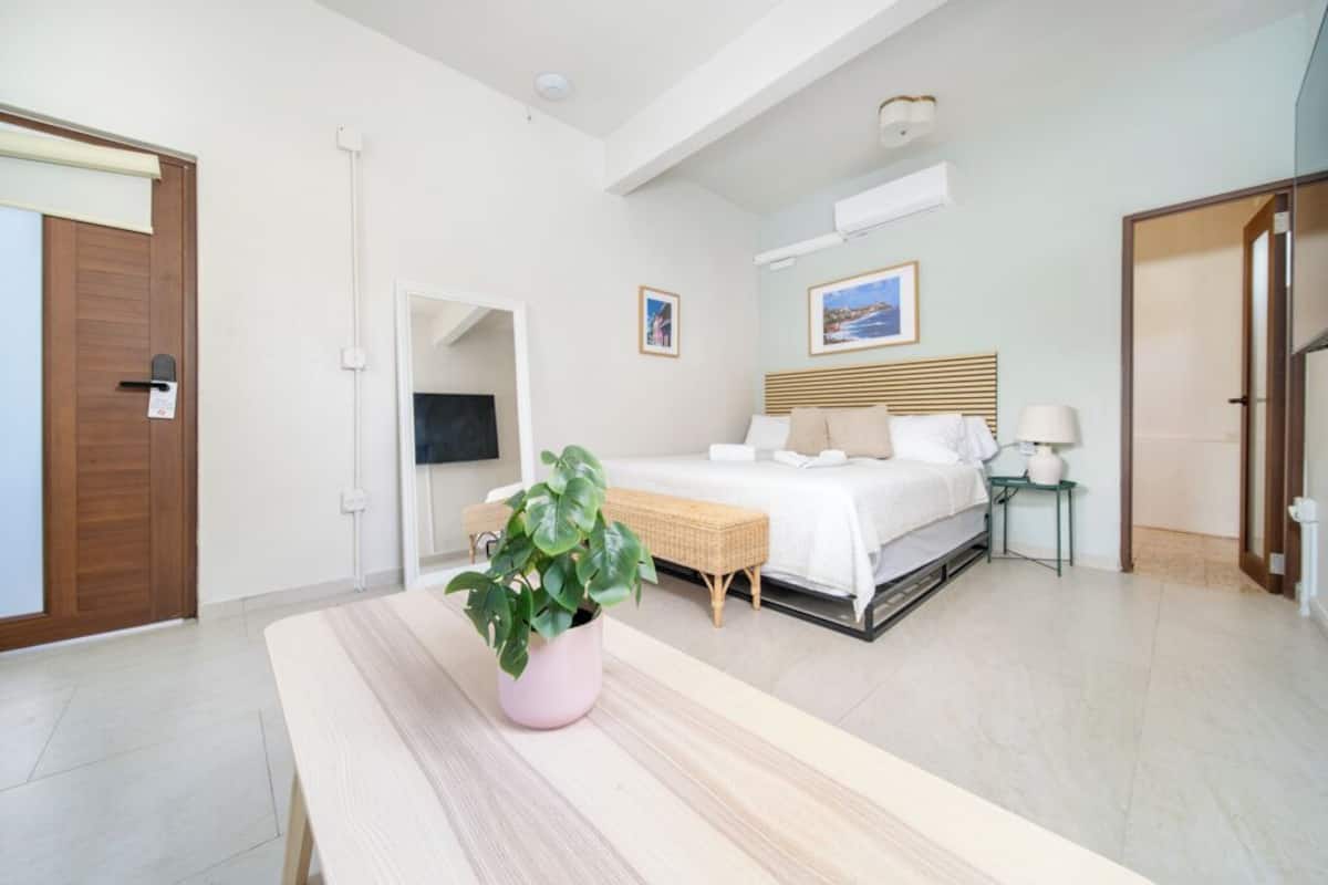 A modern bedroom with a bed, bedside table, lamp, and a potted plant.