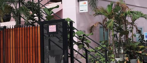 Un bâtiment rose avec un auvent vert, une entrée fermée par un portail et une enseigne indiquant un hall d'entrée.