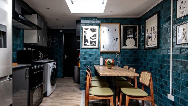 A compact kitchen with modern appliances, a dining area with a wooden table and chairs, and a wall adorned with framed artwork. - 82A Dalston Lane Terrace (London)