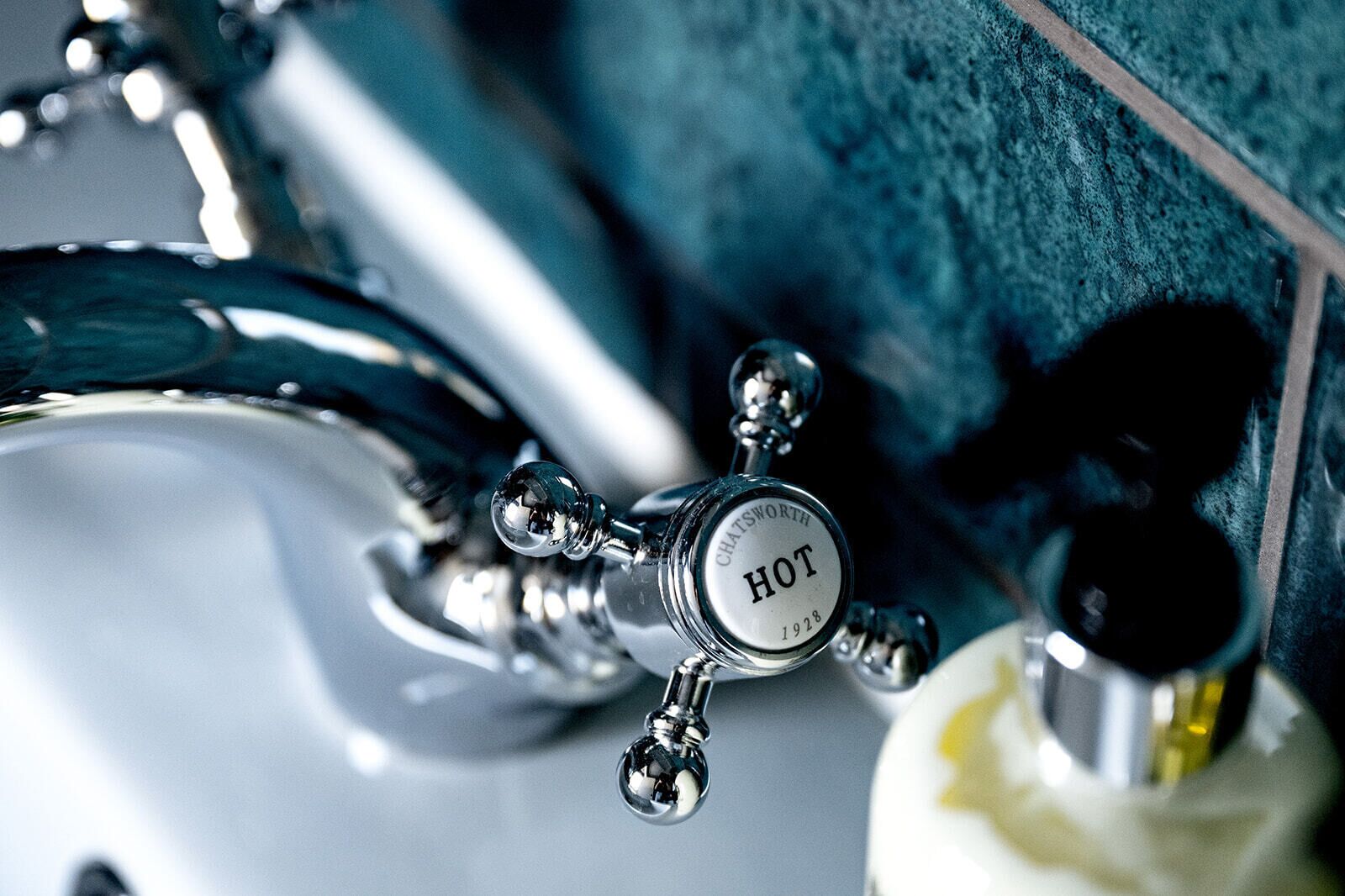 A bathroom sink with a chrome faucet labeled "HOT" and a soap dispenser.