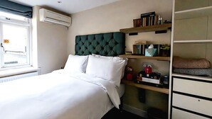 A hotel room with a bed, a headboard, a shelf with books and a clock, and a window with blinds. - 82A Dalston Lane Terrace (London)