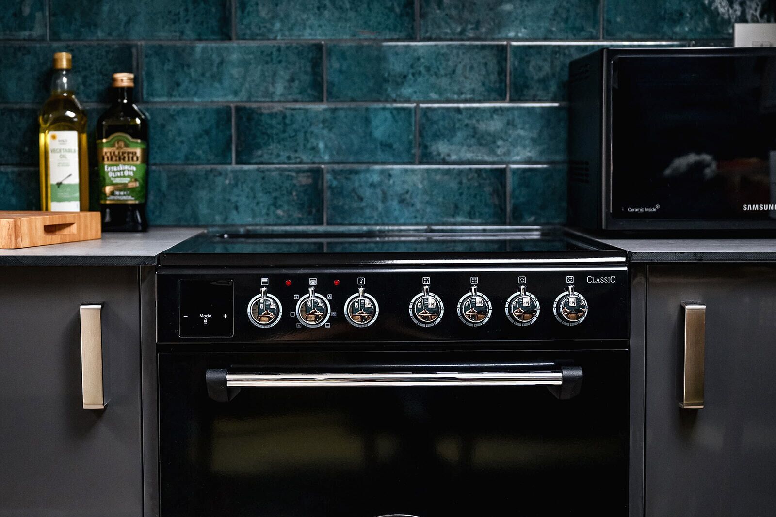 Una cocina con estufa negra, microondas y dos botellas de aceite de oliva sobre la encimera.